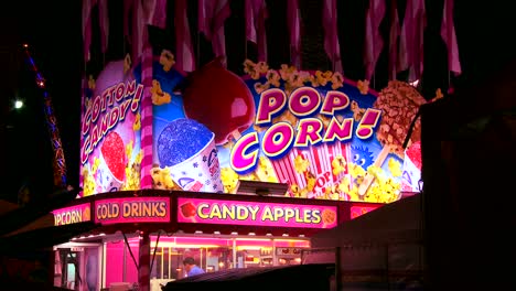 establishing shot of a food stall offering popcorn and candy apples at an amusement park carnival or state fair at night