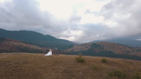 Lovely-young-newlyweds-bride-groom-walking-on-mountain-slope,-aerial-view,-wedding-couple-family