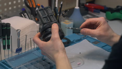 male worker tightens screws in cinema lens in workshop