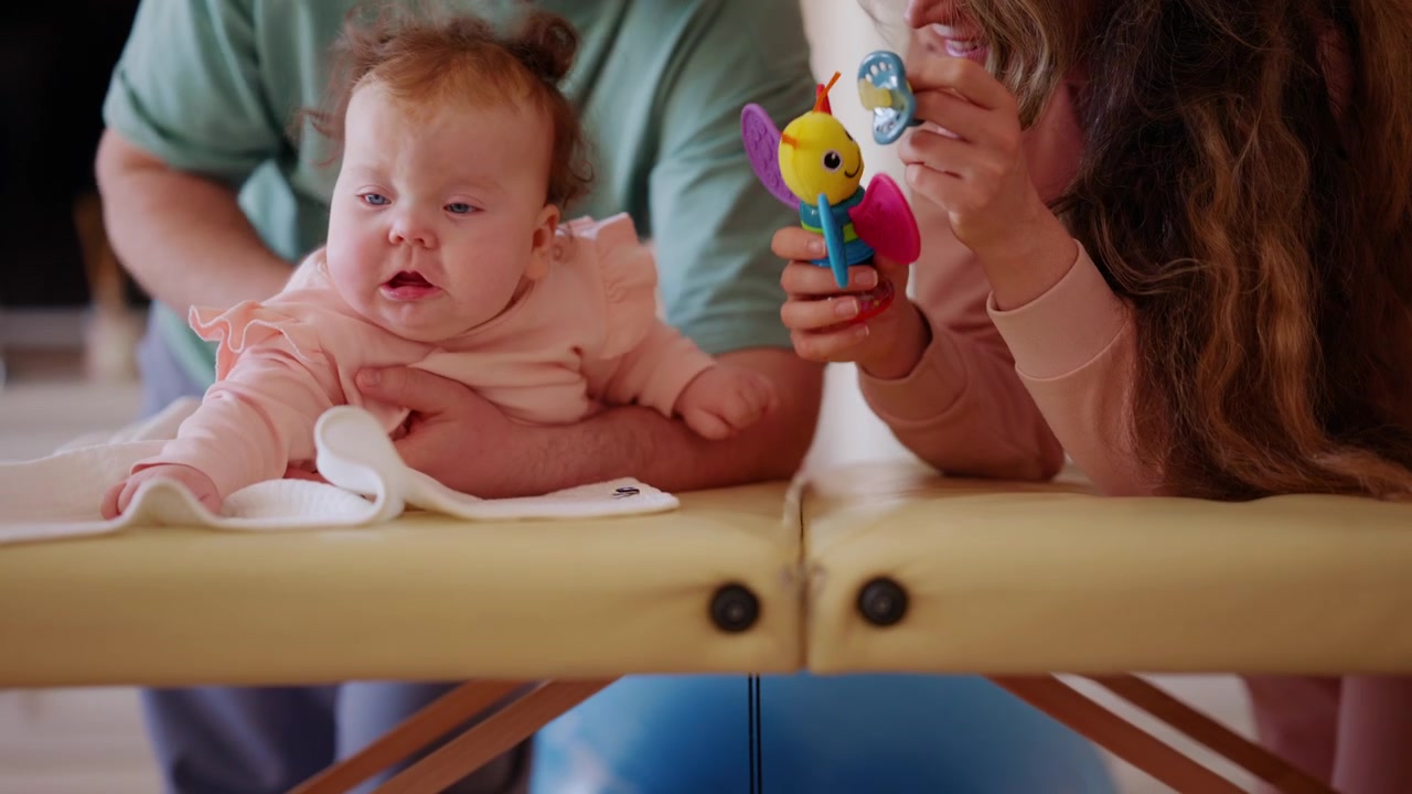 A baby lies comfortably while watching a colorful toy, and doing mobility exercises with a caregiver