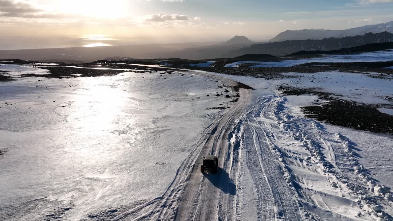 A vehicle traversing a snowy and icy road through a rugged winter landscape with mountains and a bright sun