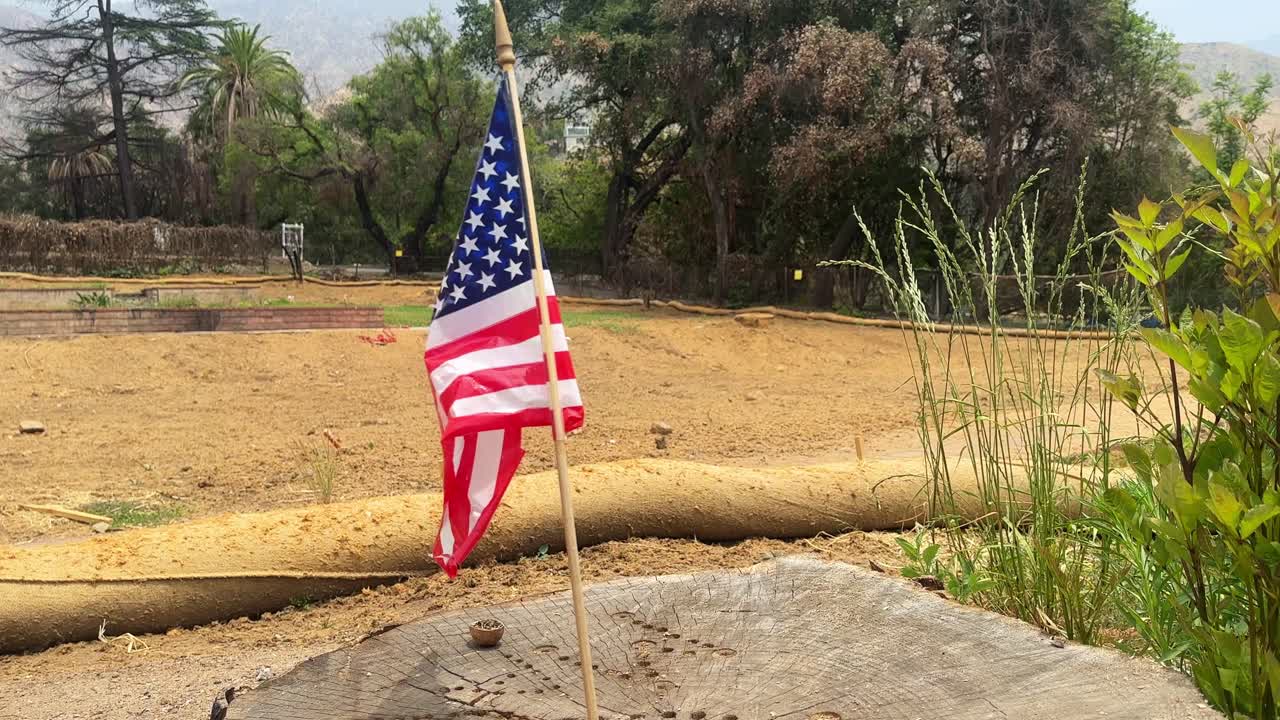 Handheld wide panning shot of an American flag flying over a residential lot burned by the wildfire in Pacific Palisades, California. 4K