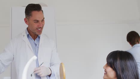 Smiling-caucasian-male-dentist-talking-with-female-patient-at-modern-dental-clinic