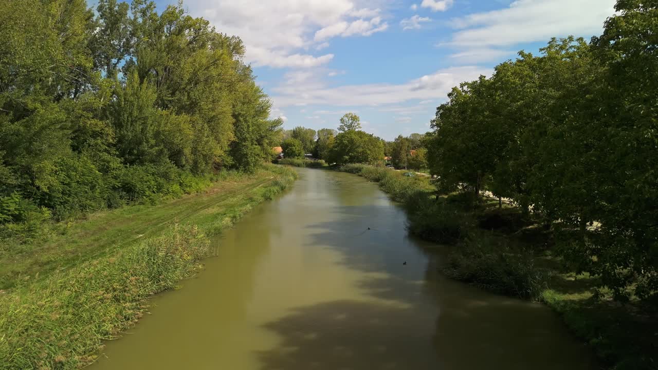 Vloeiende luchtopnames boven het kanaal in Dömsöd, Hongarije, met groene rivieroevers, kalm water en vroeg herfstblad onder een heldere hemel