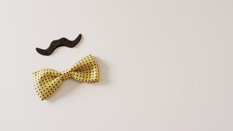 Video-of-black-false-moustache-and-yellow-spotted-bow-tie-on-white-background-with-copy-space