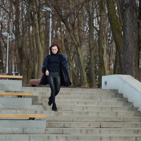 beautiful girl in the park. happy young woman goes down the stairs in the park. attractive model in fur coat. slow motion.