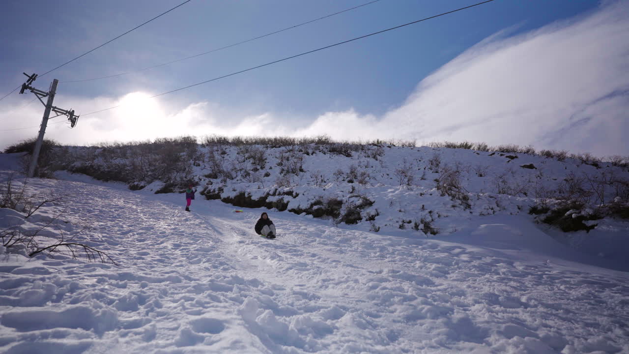 Mother sledding on snow while daughter enjoys winter holiday at ski resort in Andes