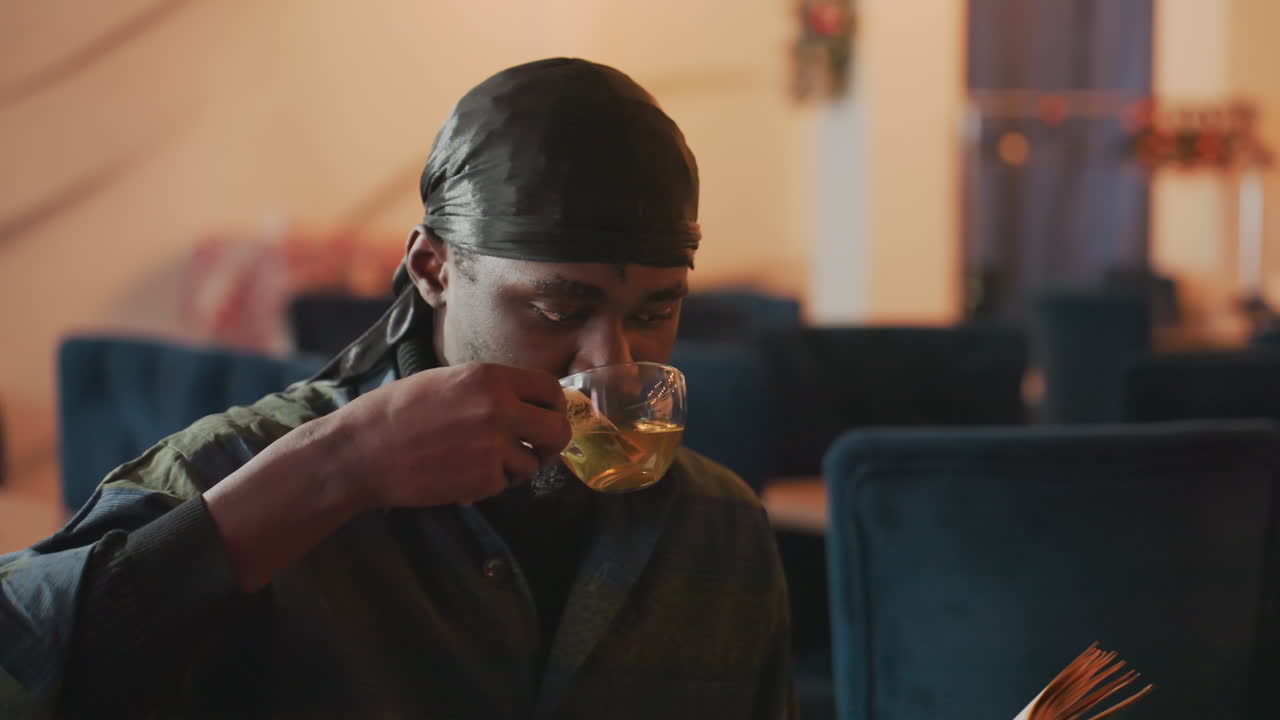student enjoys tea, young learner relaxes with beverage, individual studies comfortably in cozy cafe setting, person immersed in reading while enjoying warm tea in snug environment