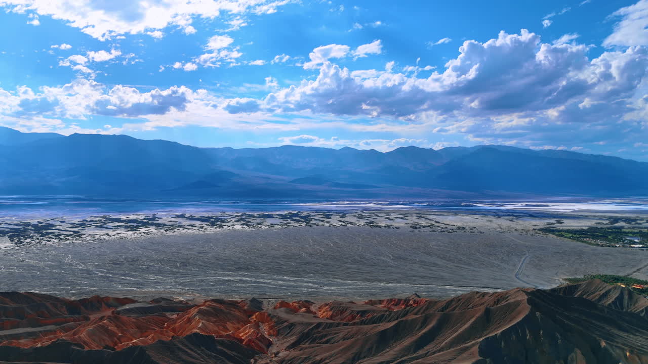 Huge deserted valley surrounded by the bare rocks. White fluffy clouds lit with bright sun in the blue sky above. Death Valley, California, USA