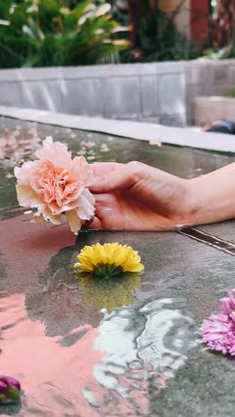 woman's hand holding pink carnation over water with yellow flower and reflections