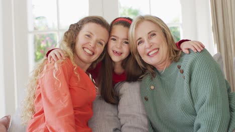 video portrait of happy caucasian mother, grandmother and granddaughter embracing on couch