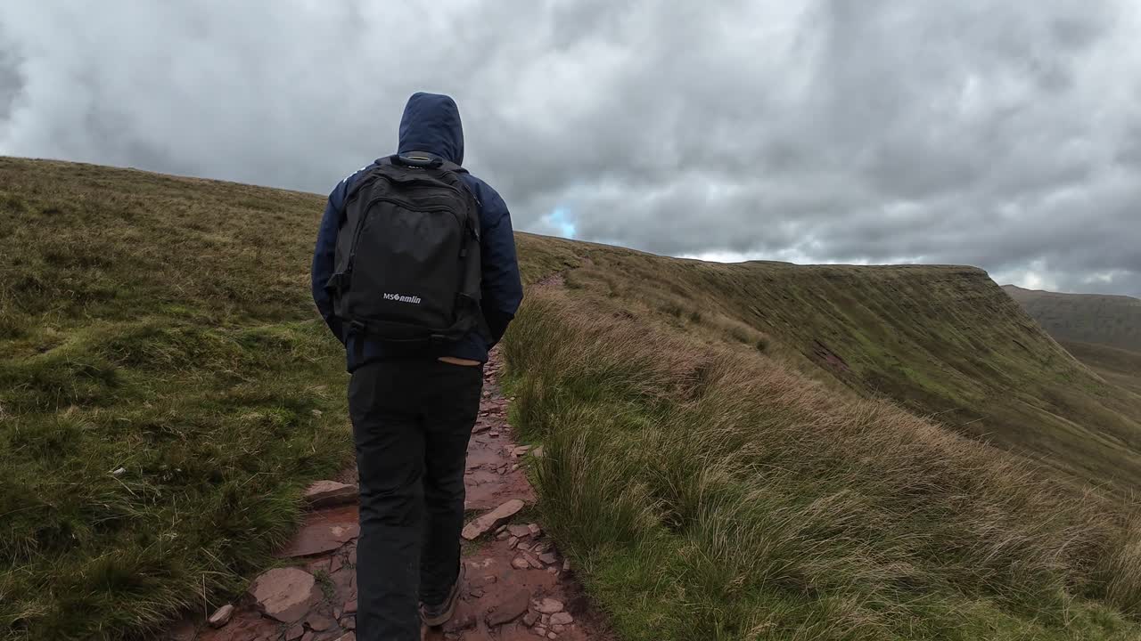 Scenic view of a man walking towards the Pen y Fan summit in Brecon Beacons National Park. Captures lush grassland, dramatic sky, and mountainous backdrop, conveying adventure and tranquility