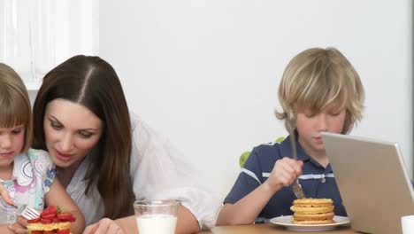 padre usando una computadora portátil y la familia comiendo un dulce en la cocina