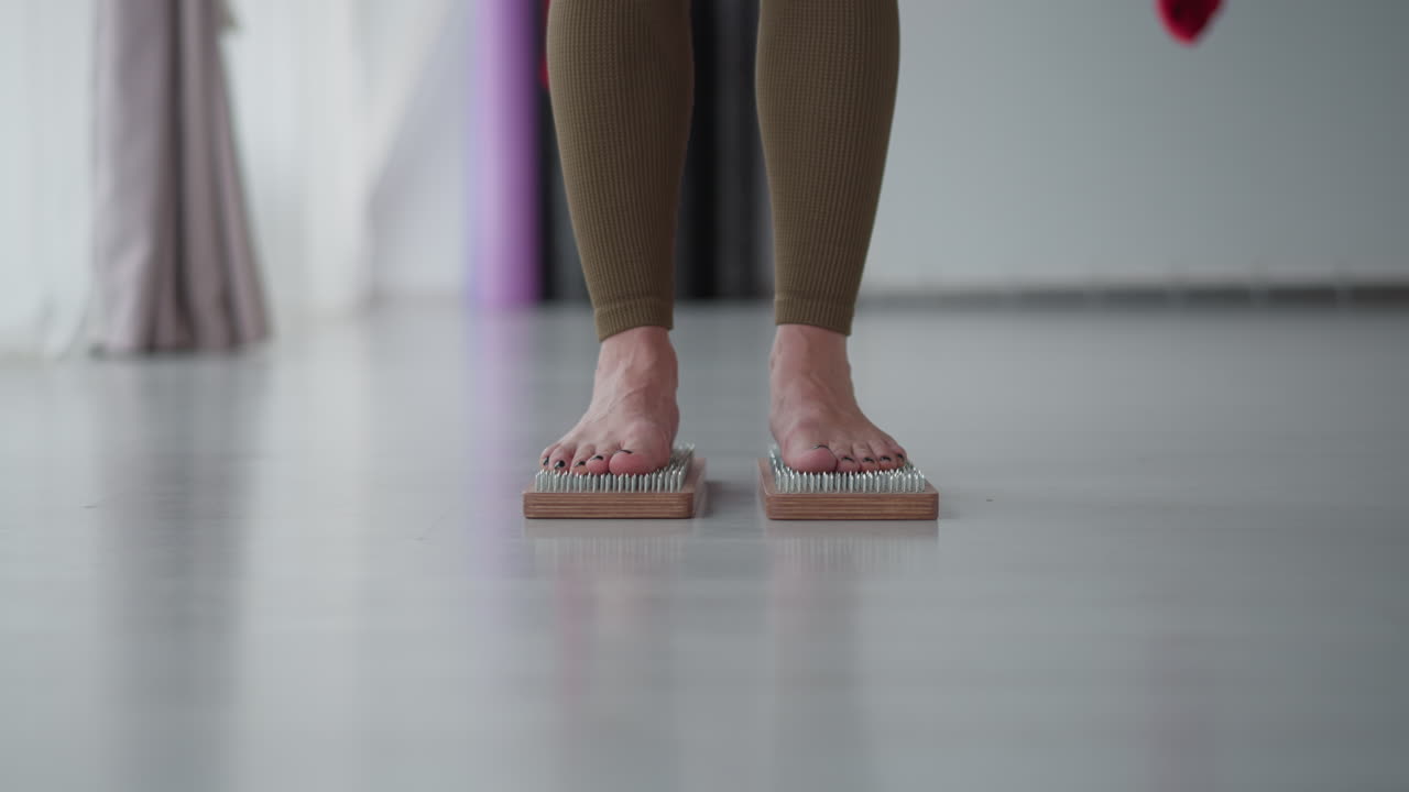 Holistic healer stands barefoot on wooden nail board inside bright studio focusing on grounding balance healing energy under soft ambient light reflecting mindful presence and body awareness