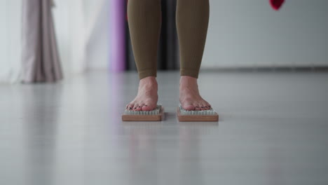 holistic healer stands barefoot on wooden nail board inside bright studio focusing on grounding balance healing energy under soft ambient light reflecting mindful presence and body awareness
