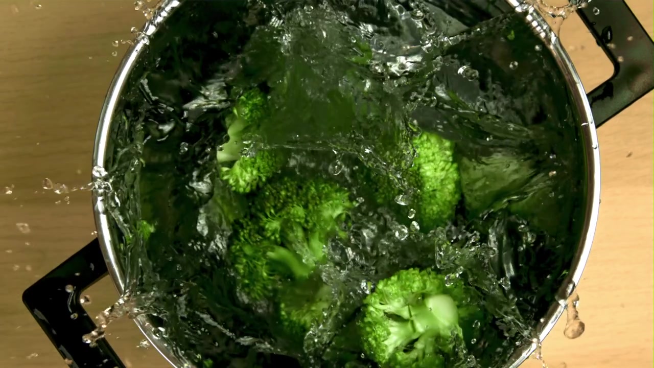 Acqua che si versa su cimette di broccoli freschi in una pentola