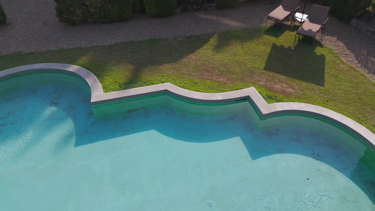 Luftfoto af en tom swimmingpool med buede kanter ved siden af et græsareal