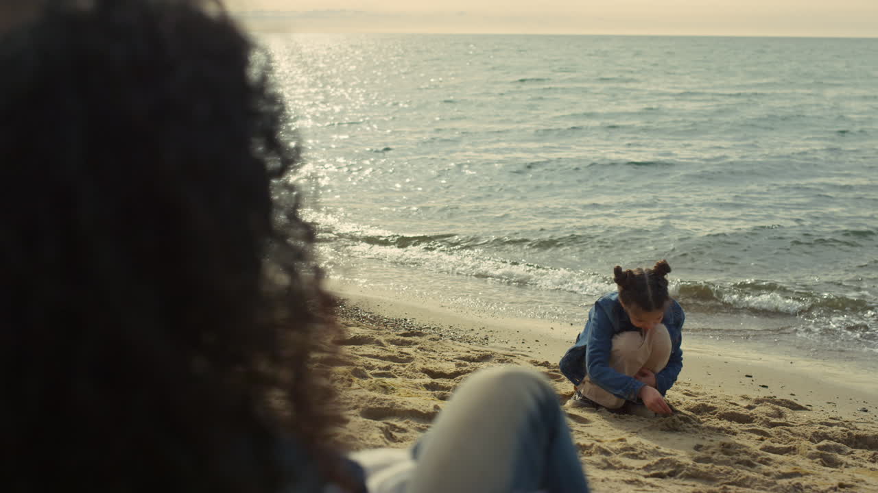 해변에 함께 앉아 있는 가족. 바쁜 아이가 바 ⁇ 가에 모래 성을 짓고 있다.