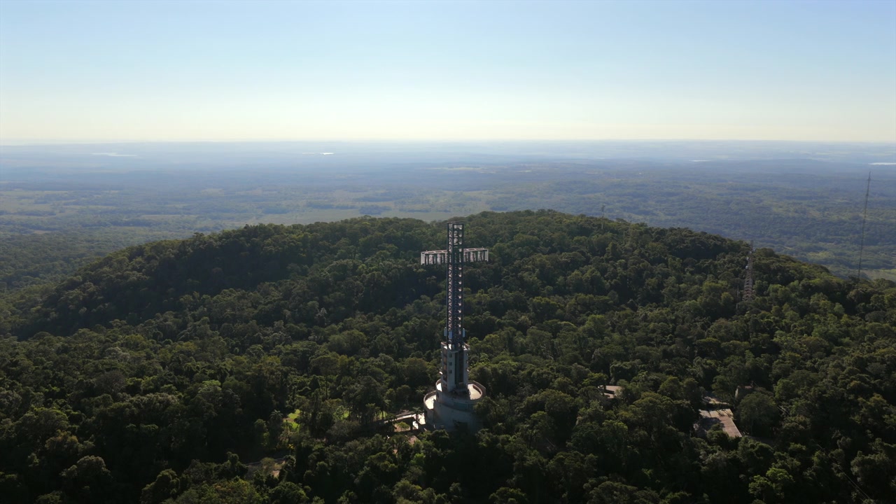 Parque Temático de la Cruz em Santa Ana, Misiones, Argentina, elevando-se acima do dossel da floresta tropical da Selva Paranaense, com paisagem subtropical panorâmica e um marco de torre de observação, em tomada aérea em órbita de drone.