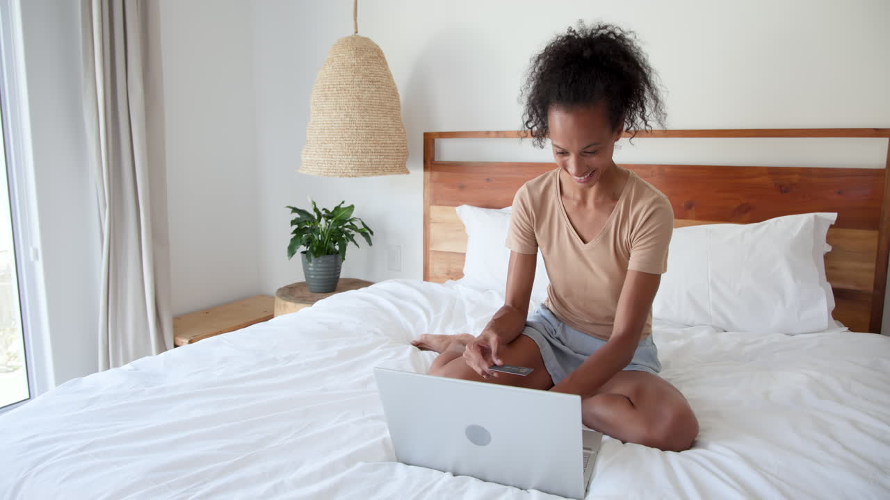 woman shopping online with laptop and credit card on bed, at home
