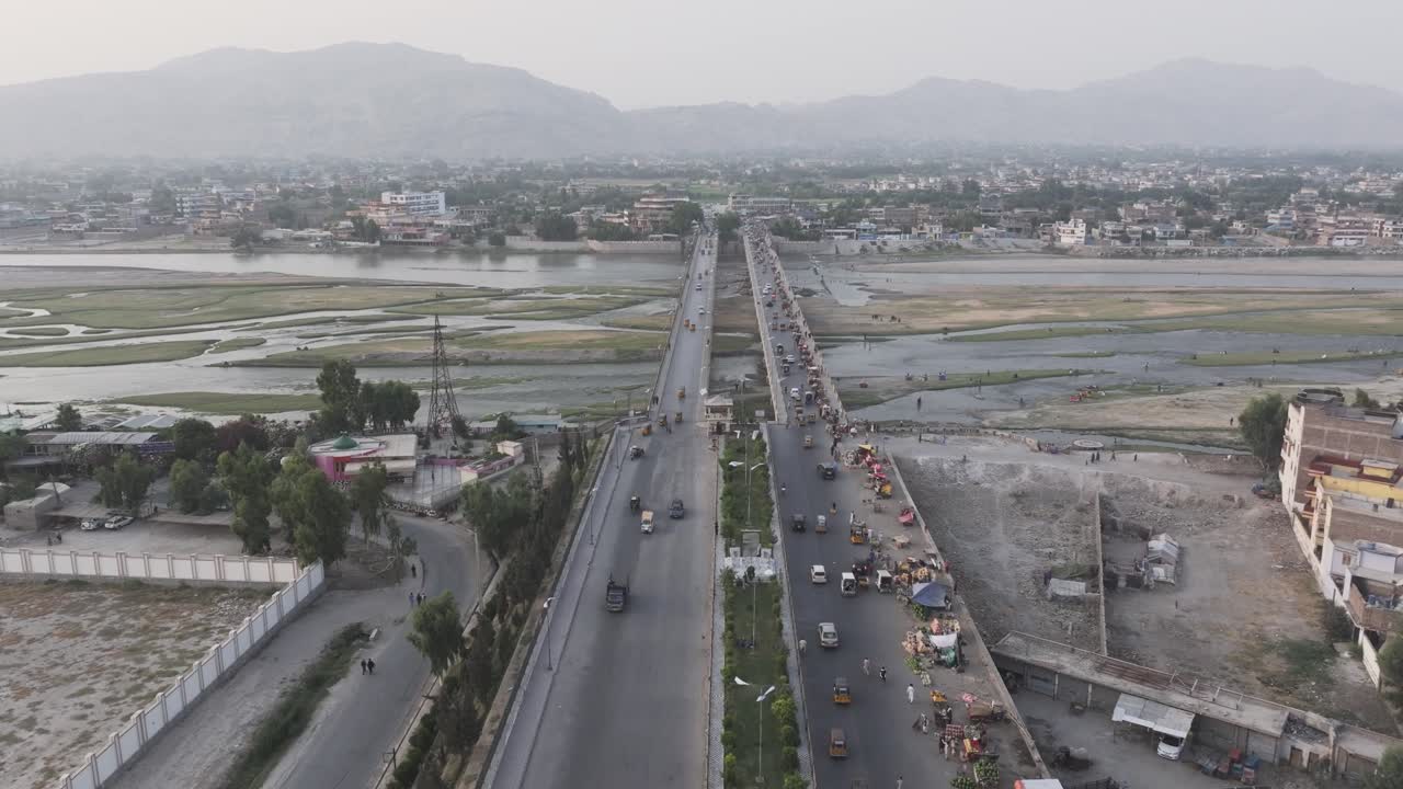 Jalalabad, Nangarhar, Afghanistan. Drone Aerial View of Bridge Traffic Above Kabul River and Buildings on Riverbanks, riverside market, solar panels on roofs, people fishing in river
