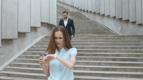 businesswoman checking time on smartwatch on street. man giving flowers woman