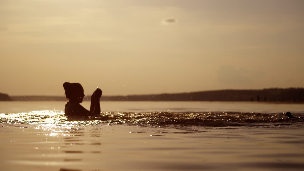 Silhouette of a woman and a boy inside the river at dusk. Mother and son making splashes on water happily in the evening.