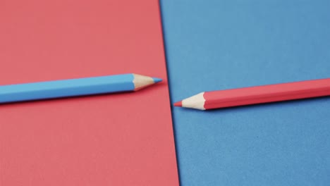 Close-up-of-blue-and-red-crayons-arranged-on-red-and-blue-background,-in-slow-motion