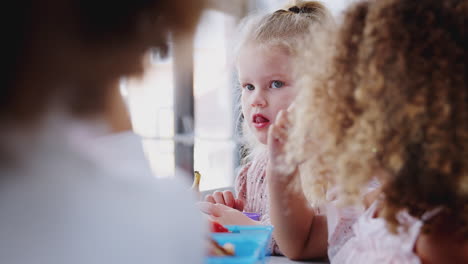 Una-Joven-Colegiala-Blanca-Comiendo-Su-Almuerzo-Para-Llevar-Con-Sus-Compañeros-De-Clase-En-La-Escuela-Infantil,-Enfoque-Selectivo