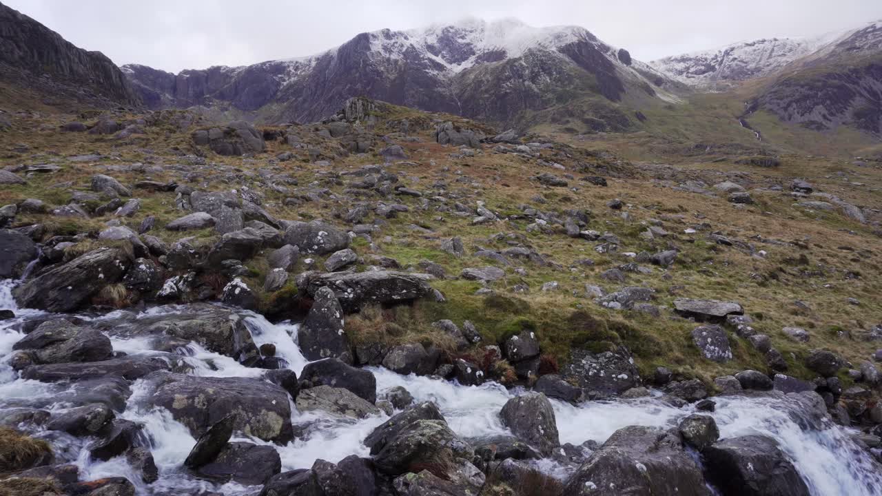arroyo que fluye a través de rocas con montañas nevadas en el norte de gales en un día nublado y ventoso