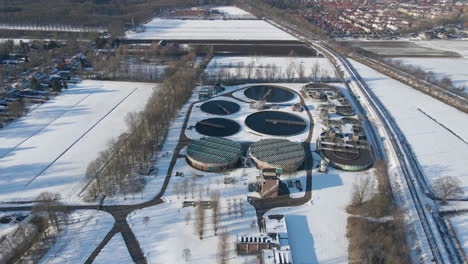 wide aerial of sewage water treatment plant in winter - drone flying backwards