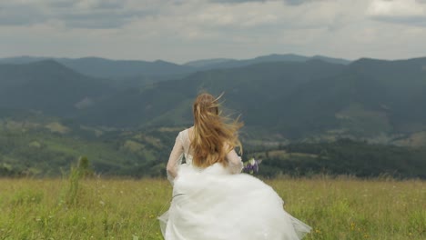 bride in white dress running through field with mountains in background