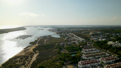 Luftpanorama-Landschaftsansicht-Von-Puerto-Marina-El-Rompido-Bei-Sonnenuntergang---Private-Immobilienhäuser,-Sandstrand,-Dock-Mit-Booten-Am-Fluss-Piedras,-Von-Steinkiefern-Umgebene-Hotels