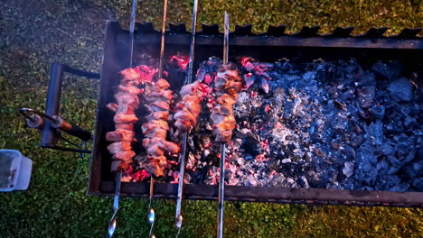 person grilling meat skewers over charcoal. - high angle shot