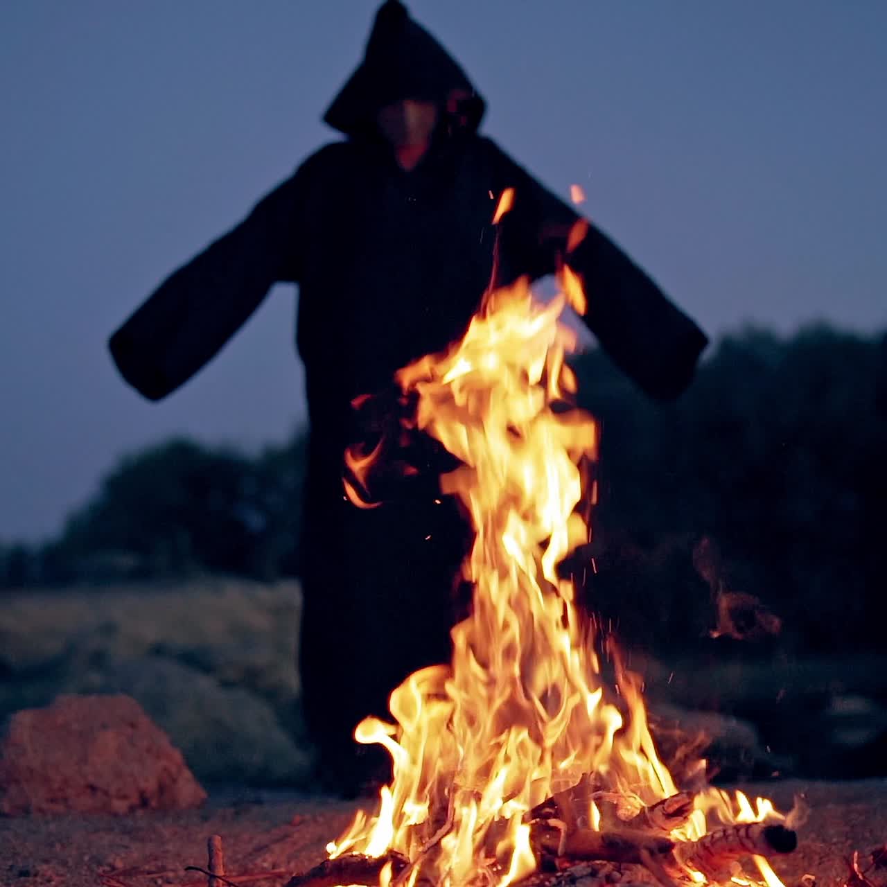 Fire flame on the dark background with black figure. Silhouette of death near the fire in the evening. Scary atmosphere at Halloween.