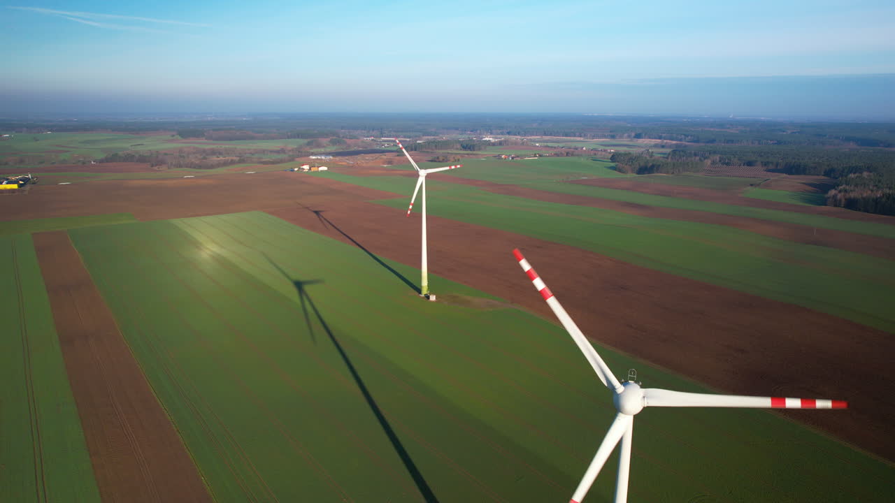 Aerial shot of energy producing wind turbines in polish country towering on green fields by the village