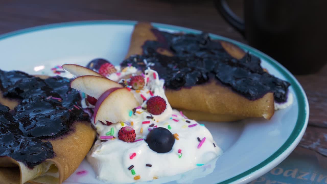 Crêpes fatte in casa ripiene di formaggio spalmabile, condite con marmellata di mirtilli, servite con panna montata e frutta fresca come mele, piccole fragole e mirtilli