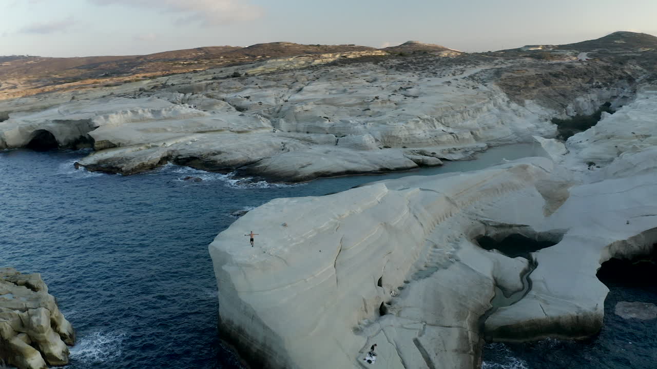 toma aérea de un dron circular de una persona en la playa desierta de sarakiniko al atardecer con una hermosa luz suave, paisaje lunar, isla de milos, grecia