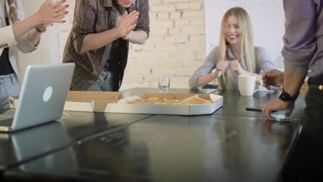 beautiful woman brings a pizza to the office. happy business colleagues sharing pizza after having a long office day