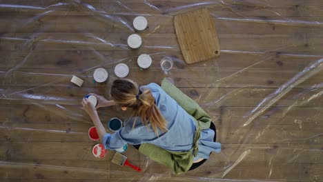 mujer en el estudio abrir diferentes colores de pintura en frascos de metal en el suelo, vista desde arriba