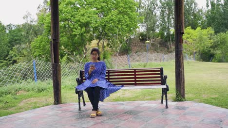 an asian girl in blue hangs up the phone and feels annoyed while lounging on a park bench