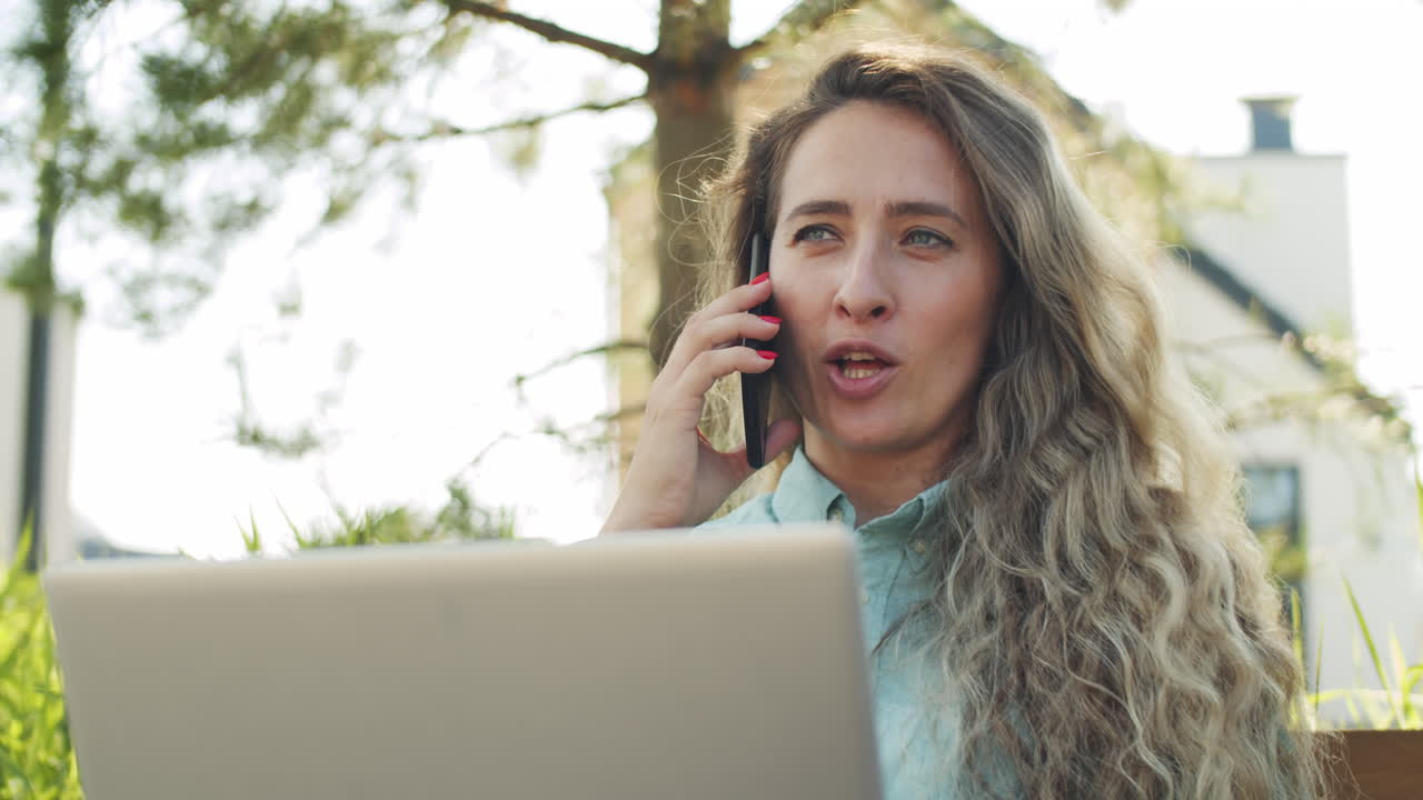 mujer de negocios alegre hablando por teléfono y usando una computadora portátil en el parque