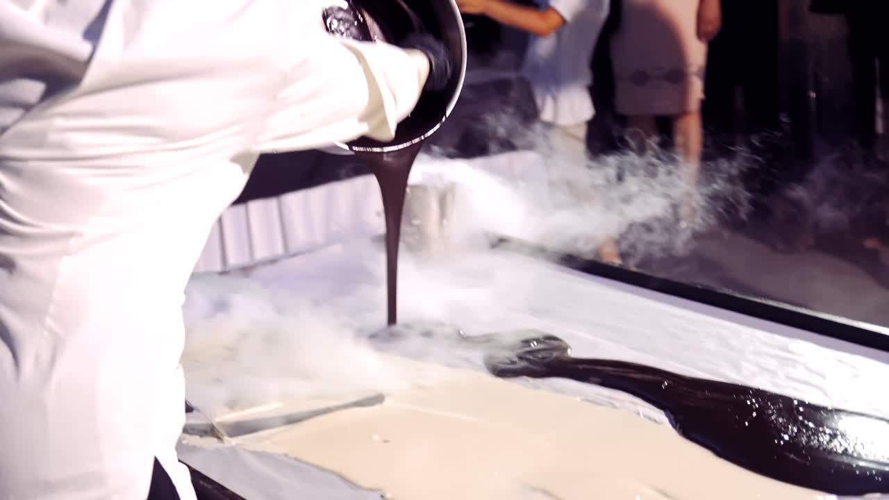 Professional cook pouring white and black liquid of cream on surface with vapoup. Chef is making large sweet dessert for guests.
