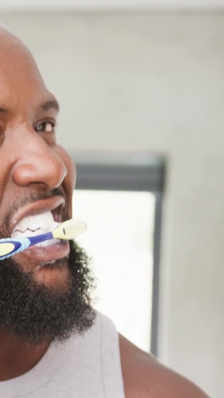 Vertical video: Brushing man in tank, blue brush entering mouth, scrubbing teeth in bathroom blind