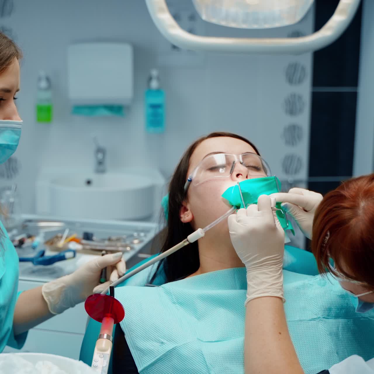 Young woman treats her sick tooth in clinic. Female dentist and assistant treating client's teeth in a modern dental office.
