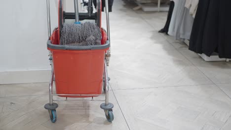 a red mop bucket with a gray mop on wheels in a store.