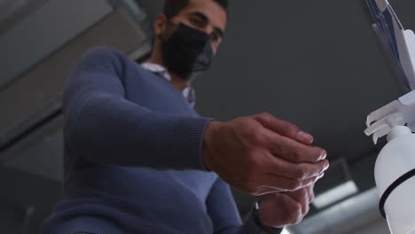 hombre de negocios con máscara facial usando desinfectante para desinfectar las manos cuando entra en el lugar de trabajo