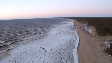 Slow-flight-above-romantic,-frozen-sea-with-pink-sky-during-early-spring-in-norther-Europe