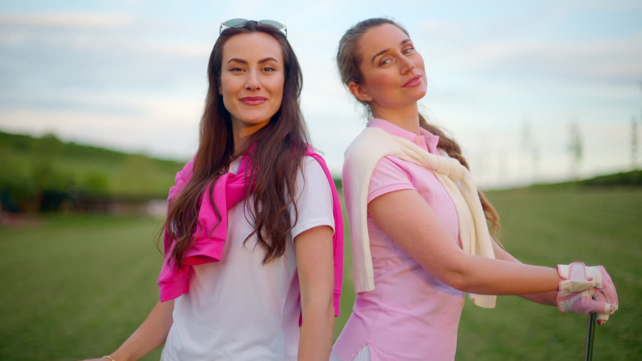 Two women in white and pink clothes, posing with golf clubs in their hands, on a grass field