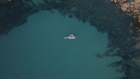 Drone-top-down-rising-above-boat-with-dinghy-and-raft-in-turquoise-green-sandy-water